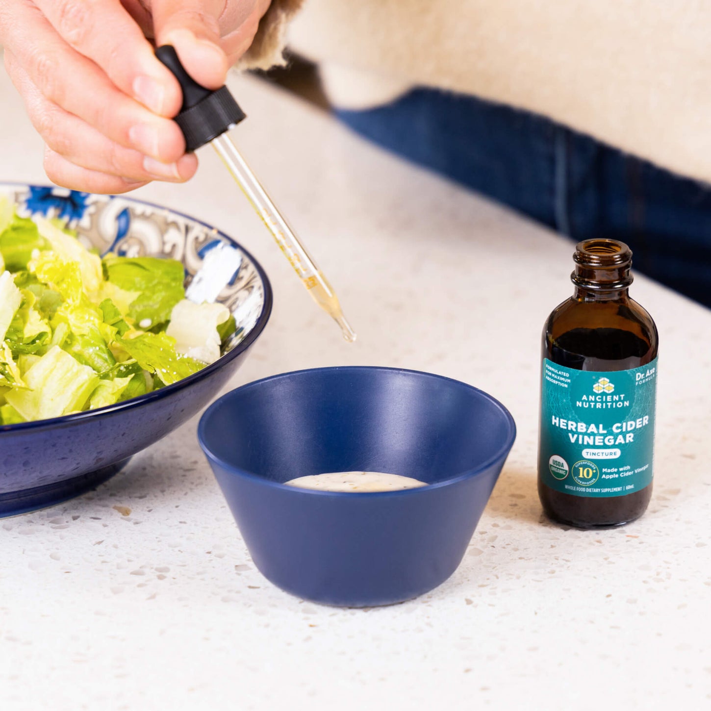 person adding dropper of herbal cider vinegar into salad dressing