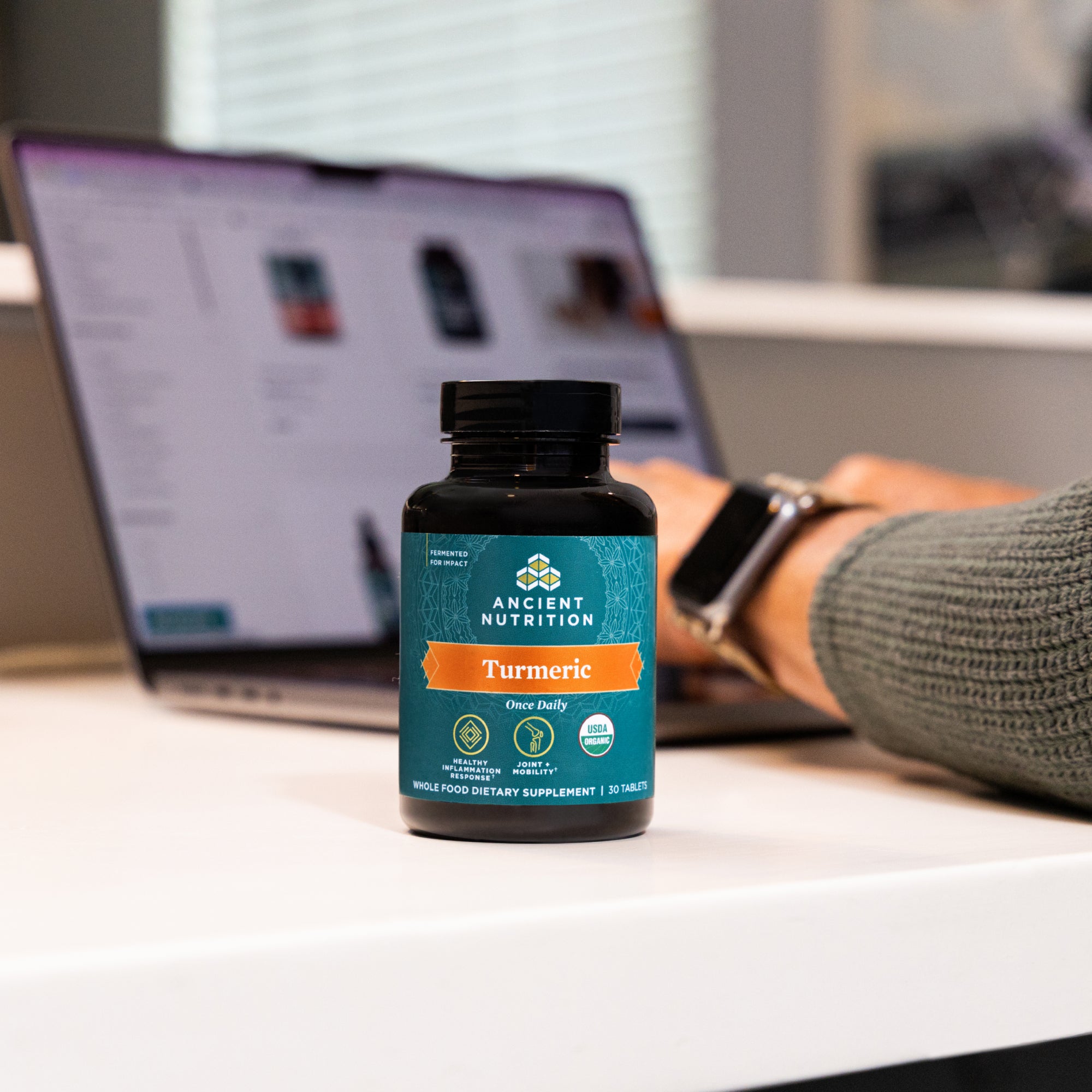 bottle of Organic Turmeric Tablets next to a person working at a computer