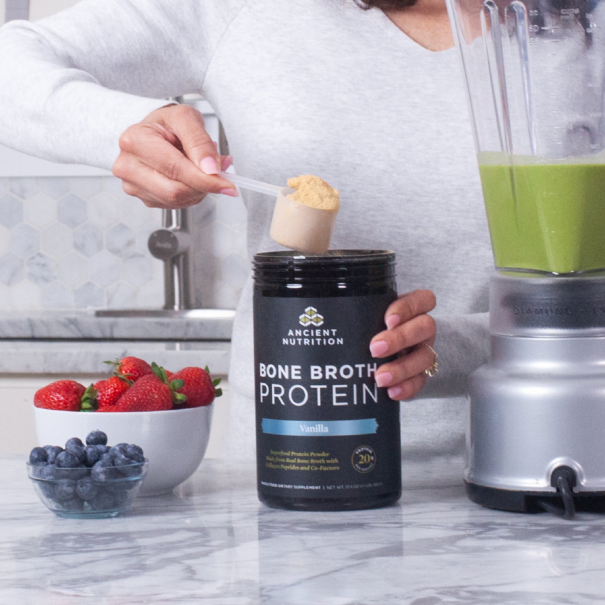 woman scooping. bone broth protein vanilla next to a bowl of fruit 